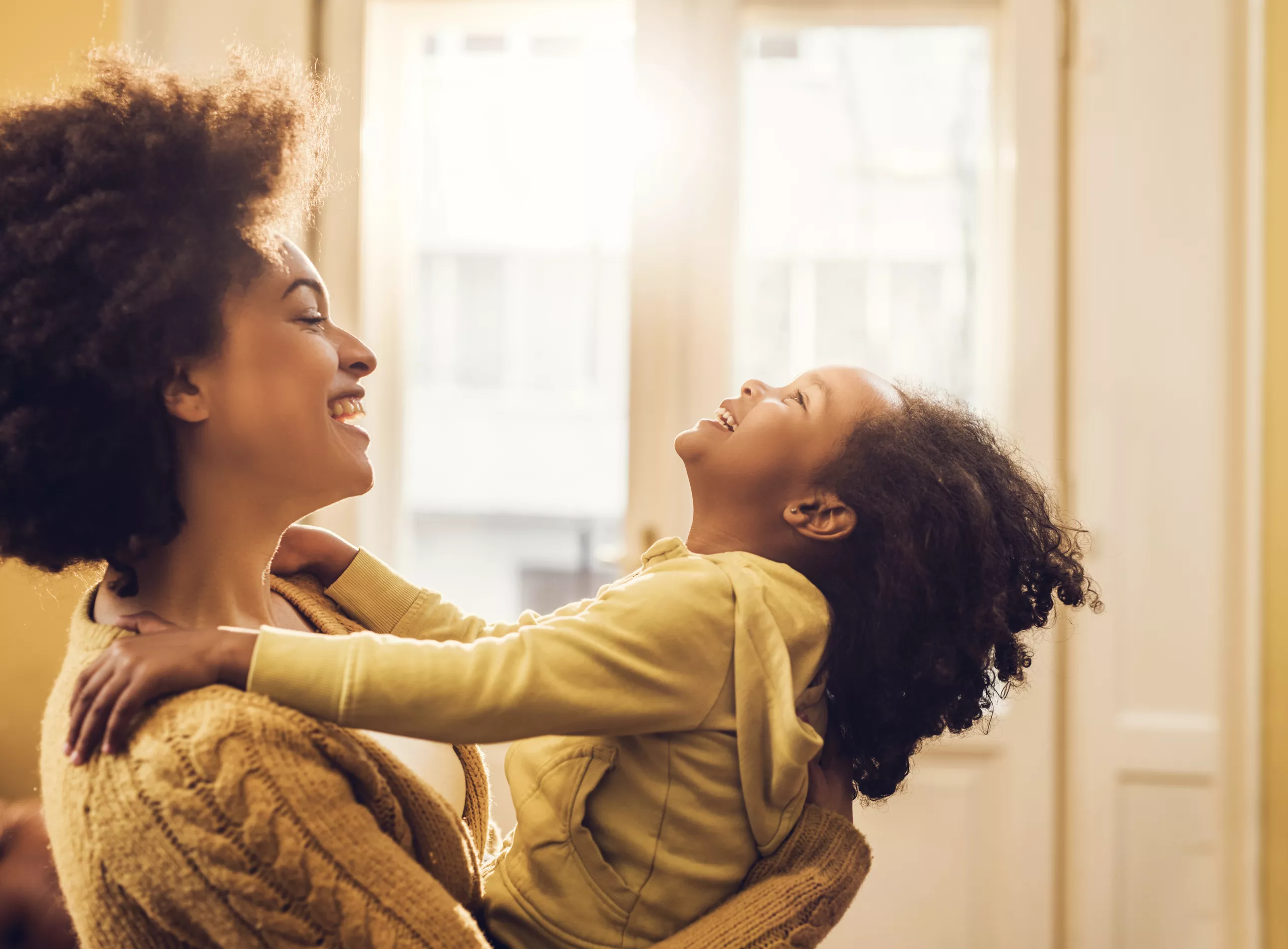 Young happy African American mother playing with her little girl at home and having fun.