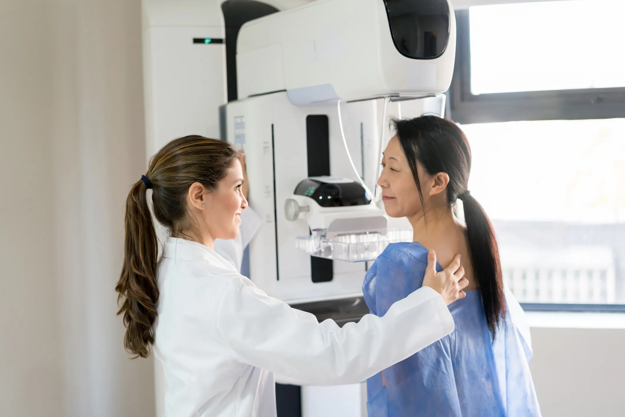 An imaging technician helps a woman getting a screening mammogram