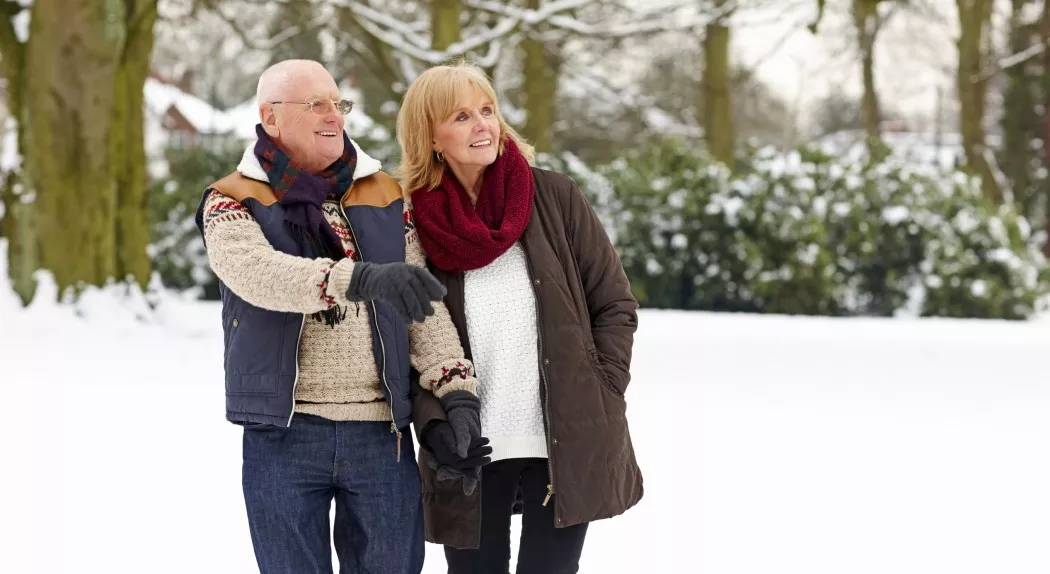 Mature couple in warm clothing walking outdoors in snow